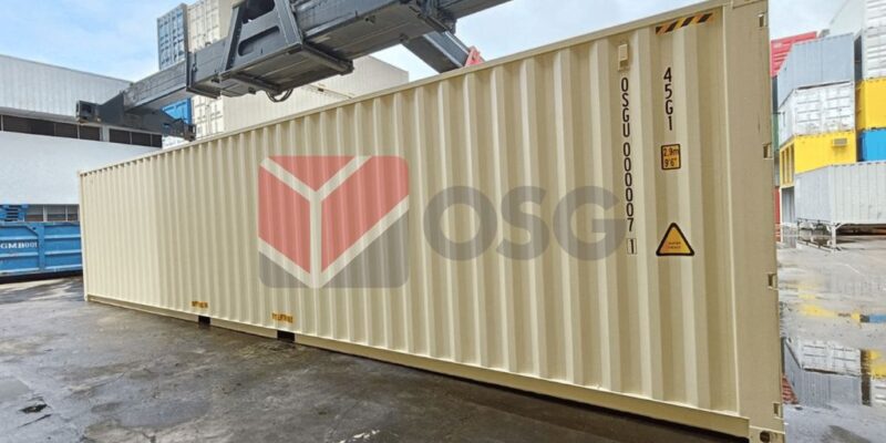 A large shipping container in a storage area, being lifted.