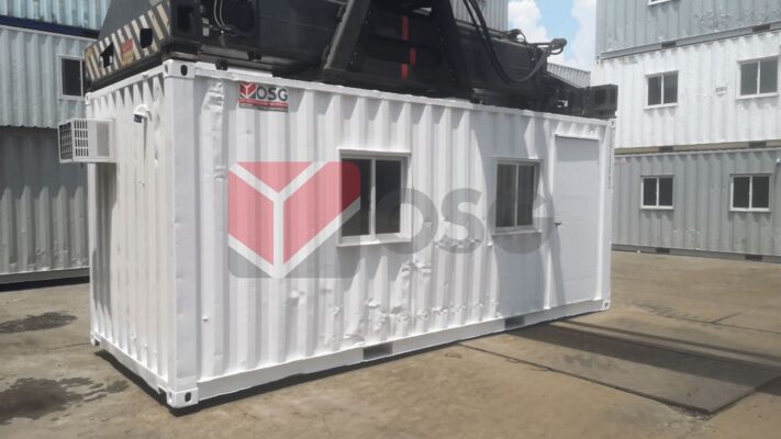 A white shipping container with windows on a construction site.