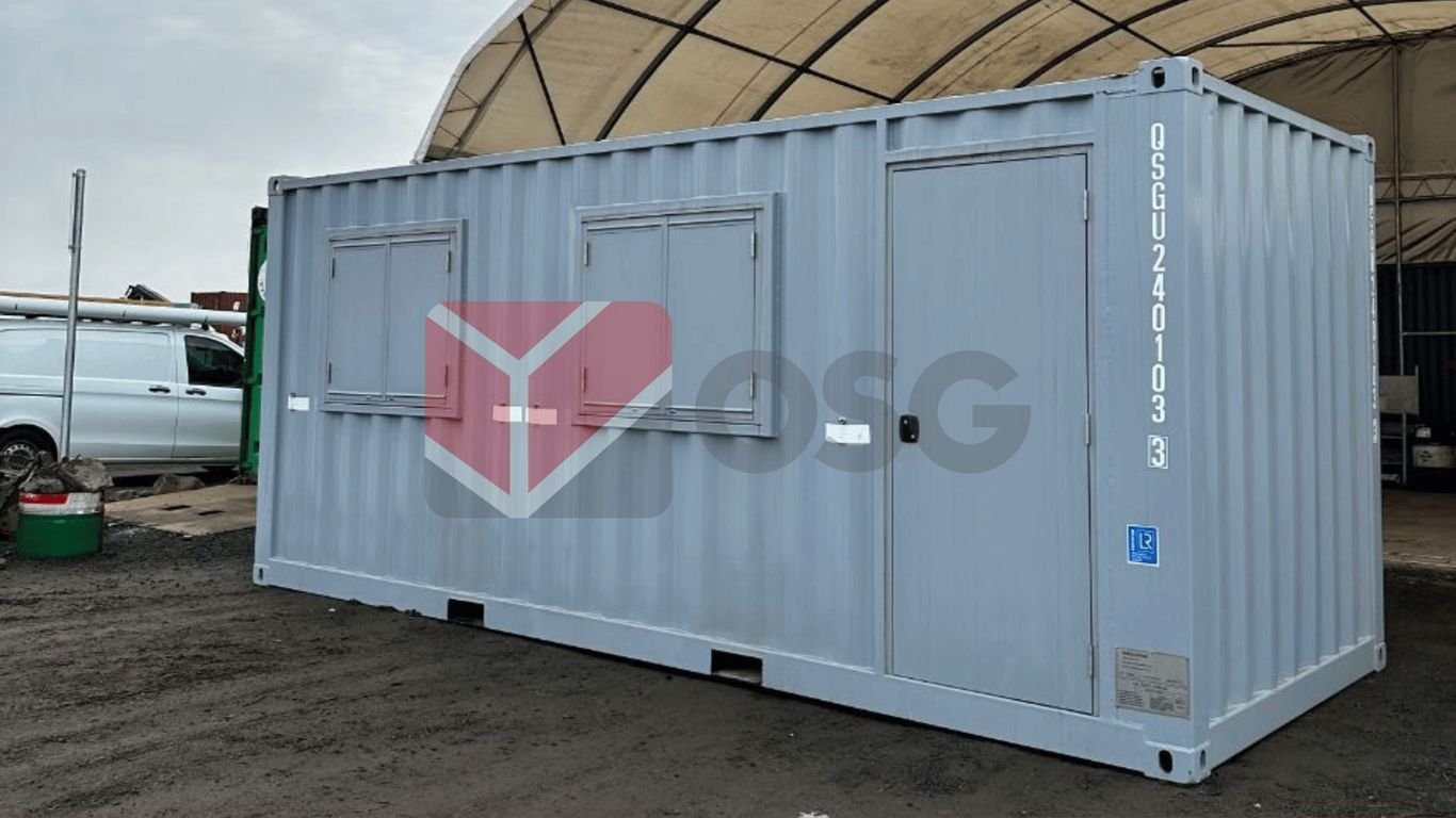 Gray shipping container with windows, located on a work site.