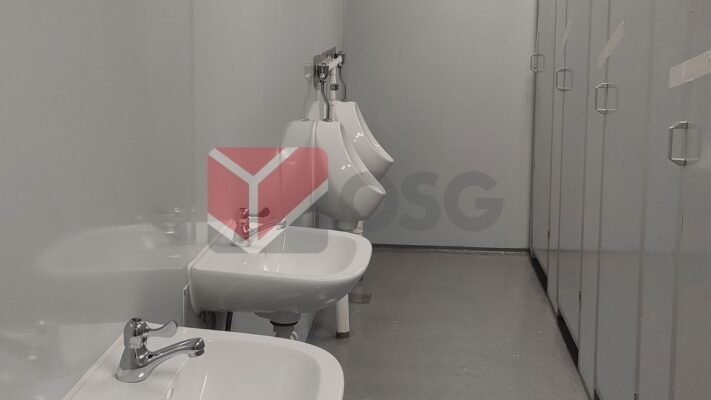 Restroom interior featuring sinks and urinals with gray walls.