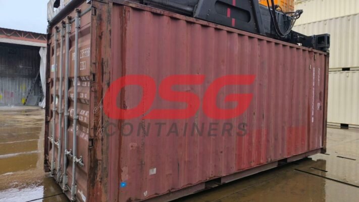 A red shipping container is being lifted by machinery.