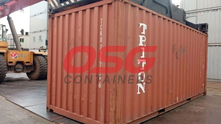 A large orange shipping container is being moved by a forklift.