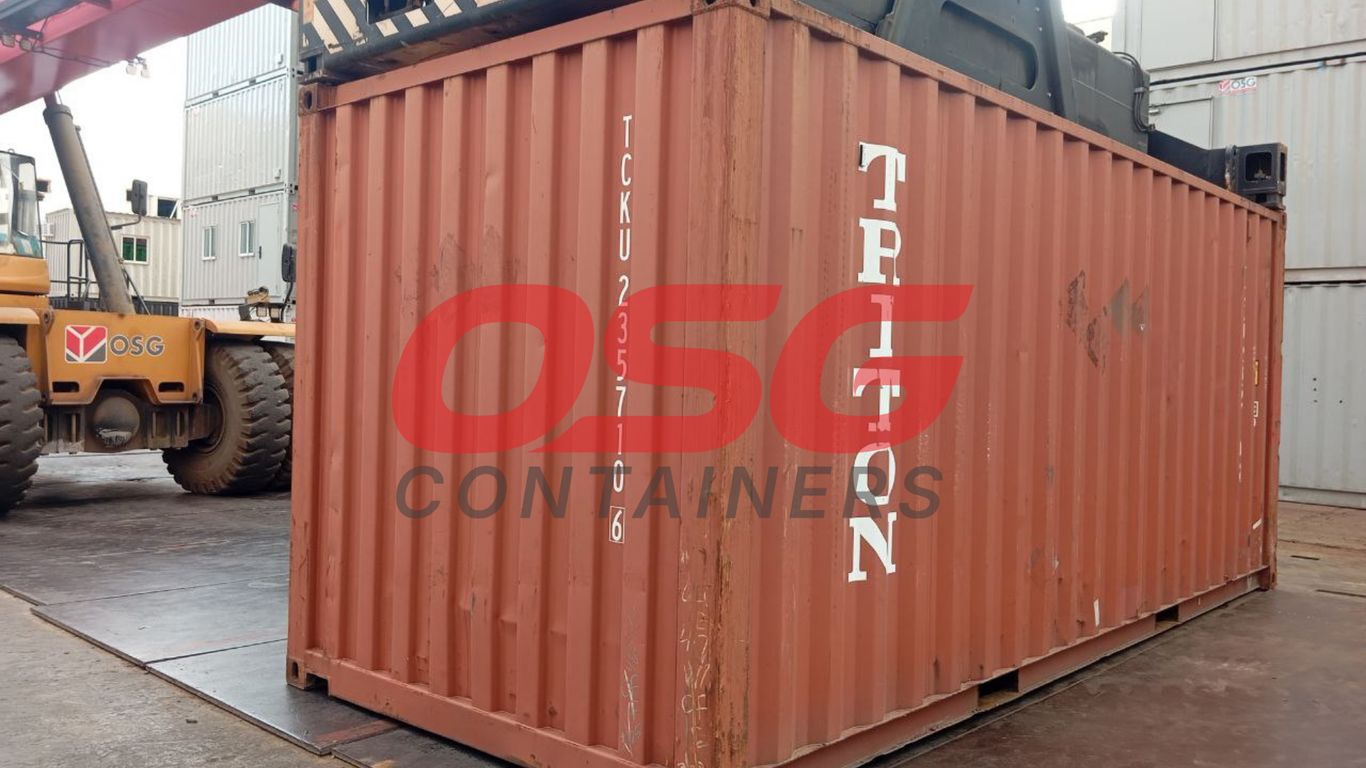 A large orange shipping container is being moved by a forklift.