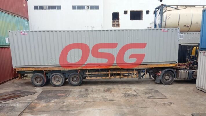 A large gray shipping container is loaded onto a truck.