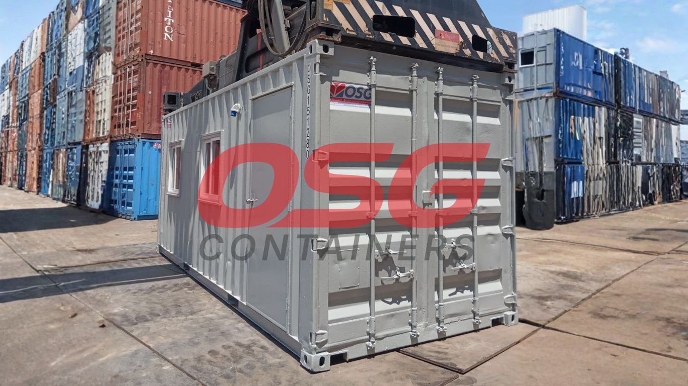 A gray shipping container office with other containers stacked around.