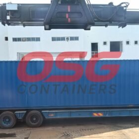 A large blue shipping container is being loaded onto a trailer.