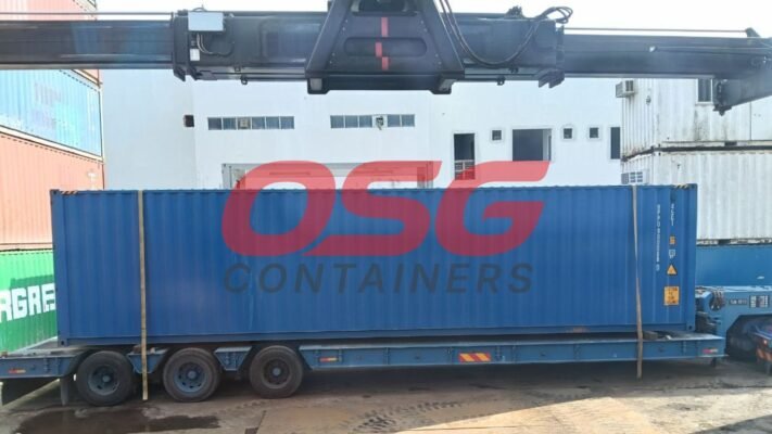 A large blue shipping container is being loaded onto a trailer.