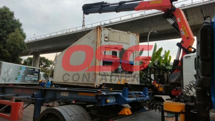 Crane lifting a refrigerated shipping container onto a truck.