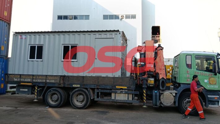 A truck with a crane is carrying a portable office container.