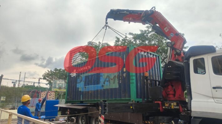 Crane truck lifting a shipping container at a construction site.