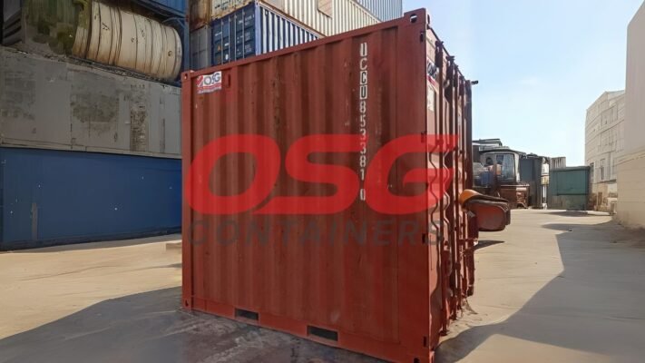 Red shipping container in a yard with other containers.