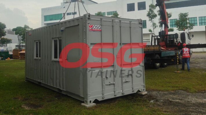 A crane is lifting a portable office container at a construction site.