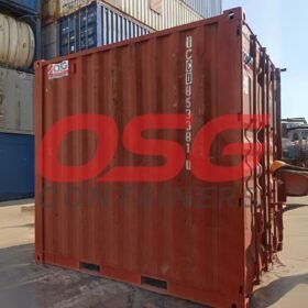 Red shipping container in a yard with other containers.