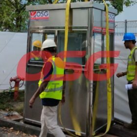 Workers installing a prefabricated security booth with yellow straps.