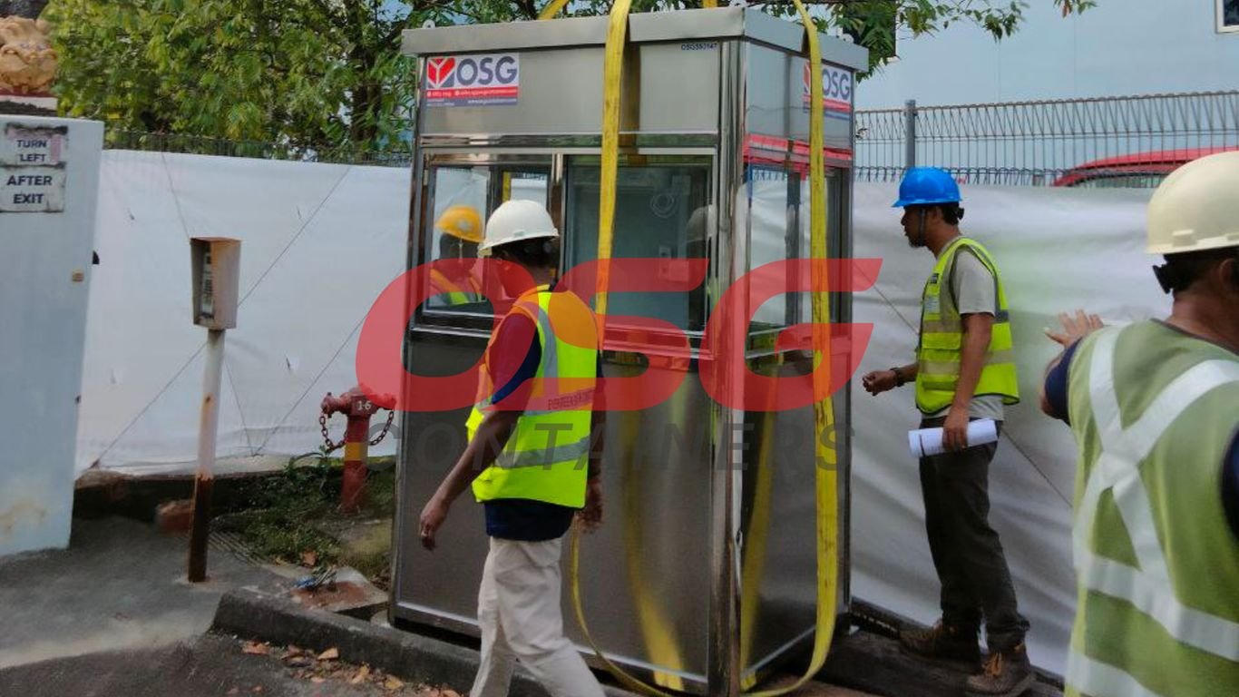Workers installing a prefabricated security booth with yellow straps.
