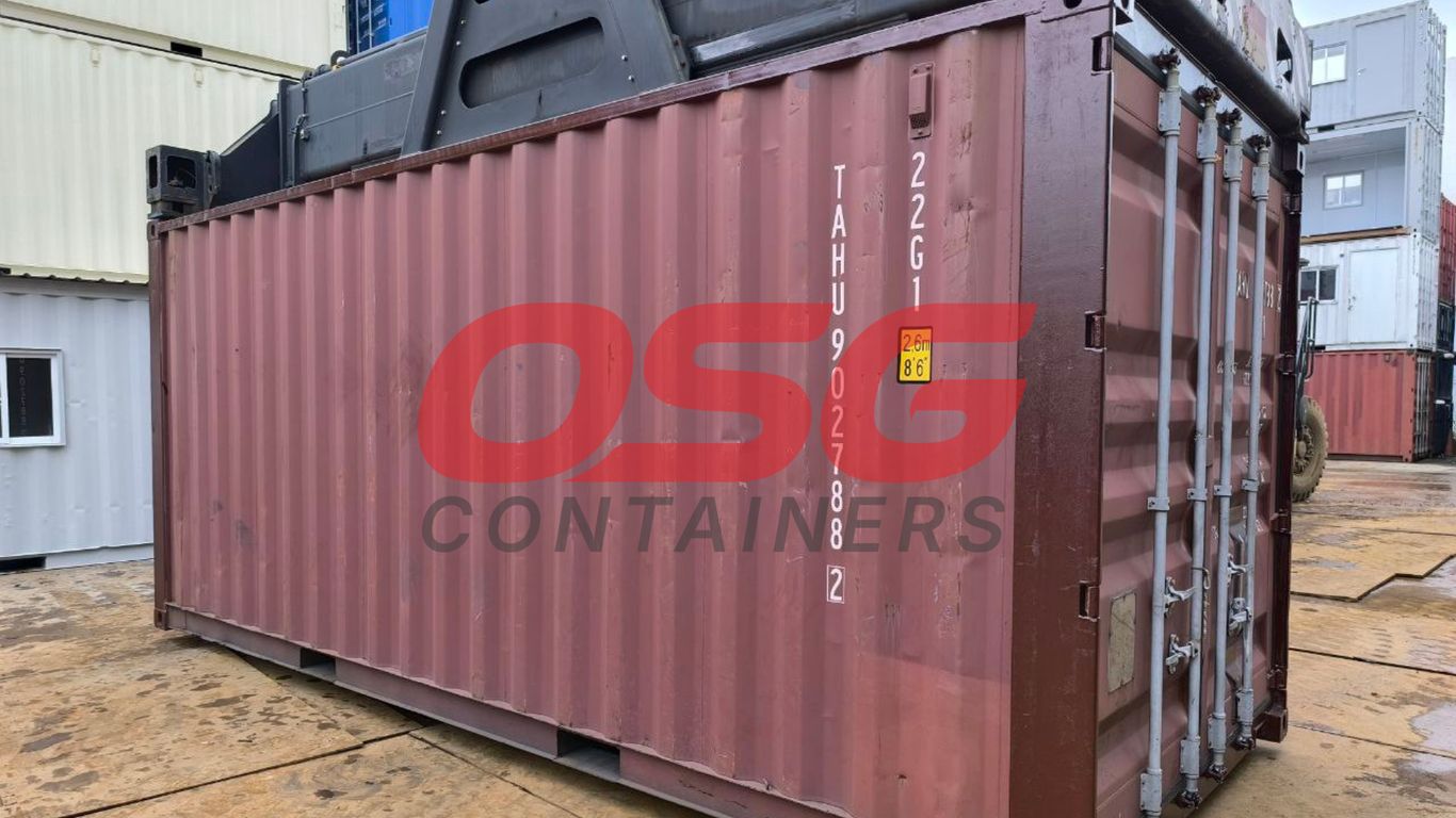 A maroon shipping container is being lifted by a crane.