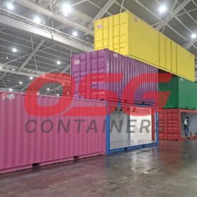 Stacked colorful shipping containers inside a large warehouse with workers.