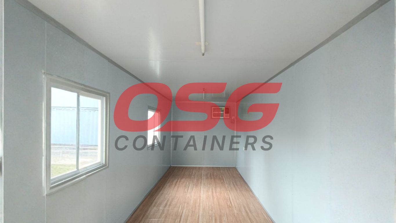Interior of an empty shipping container with a window and wood floor.