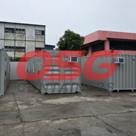Several gray shipping containers with air conditioners are parked outside.