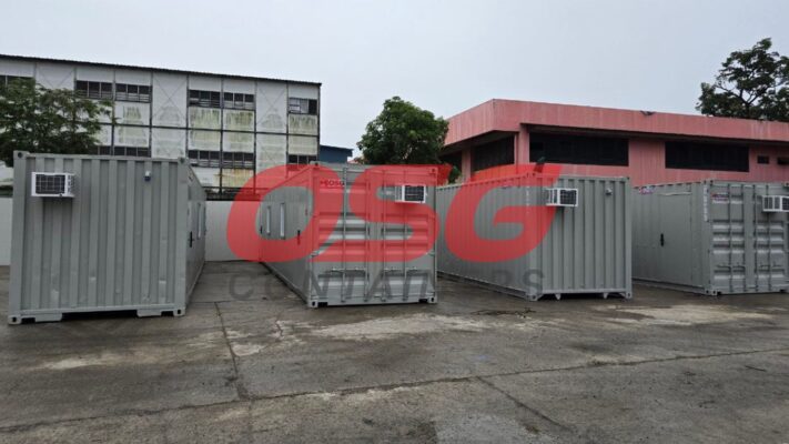 Several gray shipping containers with air conditioners are parked outside.