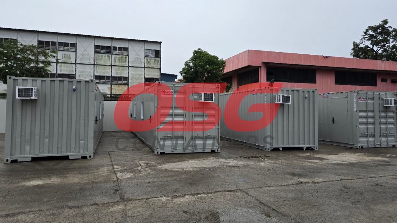 Several gray shipping containers with air conditioners are parked outside.