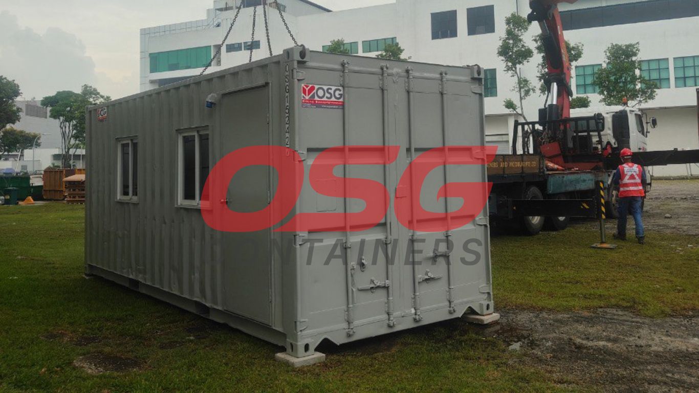 A crane is lifting a portable office container at a construction site.