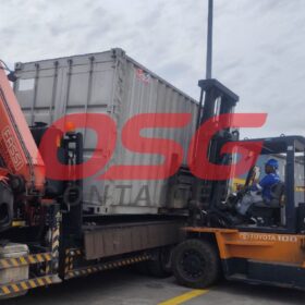 Forklift and crane loading a shipping container onto a truck.