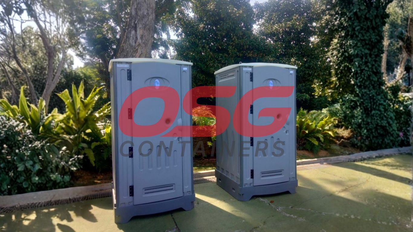 Two portable toilets are set up outdoors with lush greenery.