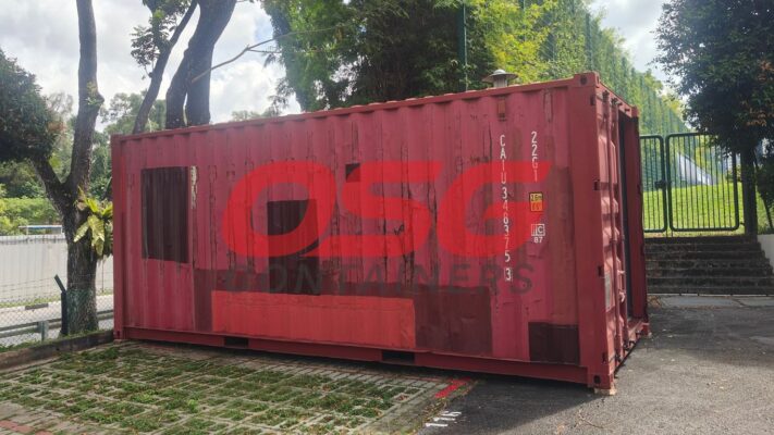 A weathered red shipping container with a large logo on its side.