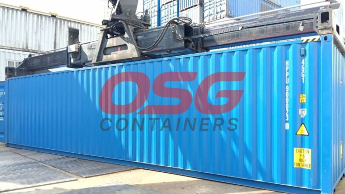 A large blue shipping container is being lifted by a crane.