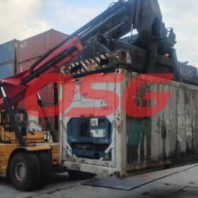 A forklift lifts a refrigerated shipping container at a port.