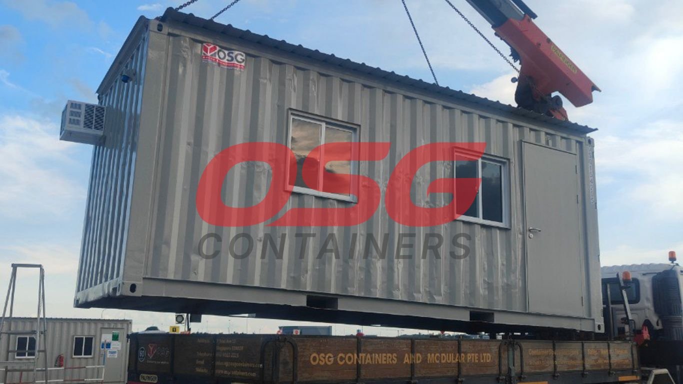 A crane lifts a modular container onto a truck.