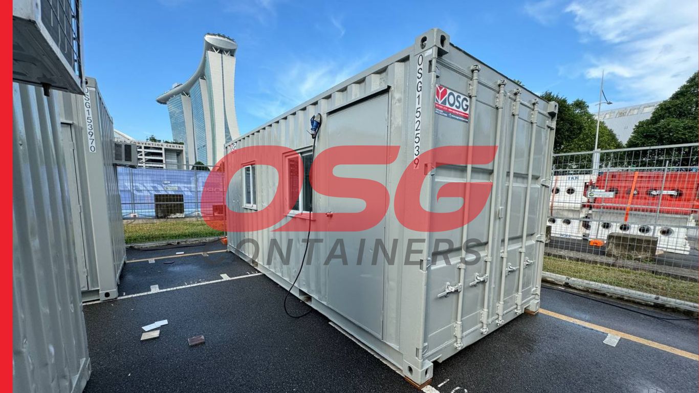 Gray shipping containers are parked in a lot with a building in the background.