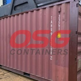 A maroon shipping container is being lifted by a crane.