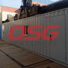 A large grey container with a crane overhead in a yard.