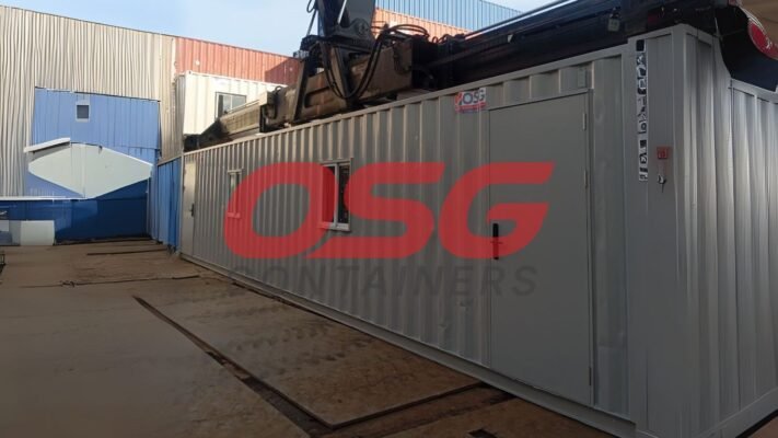 A large grey container with a crane overhead in a yard.