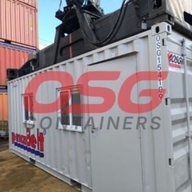 A crane lifts a modified shipping container with windows and a door.