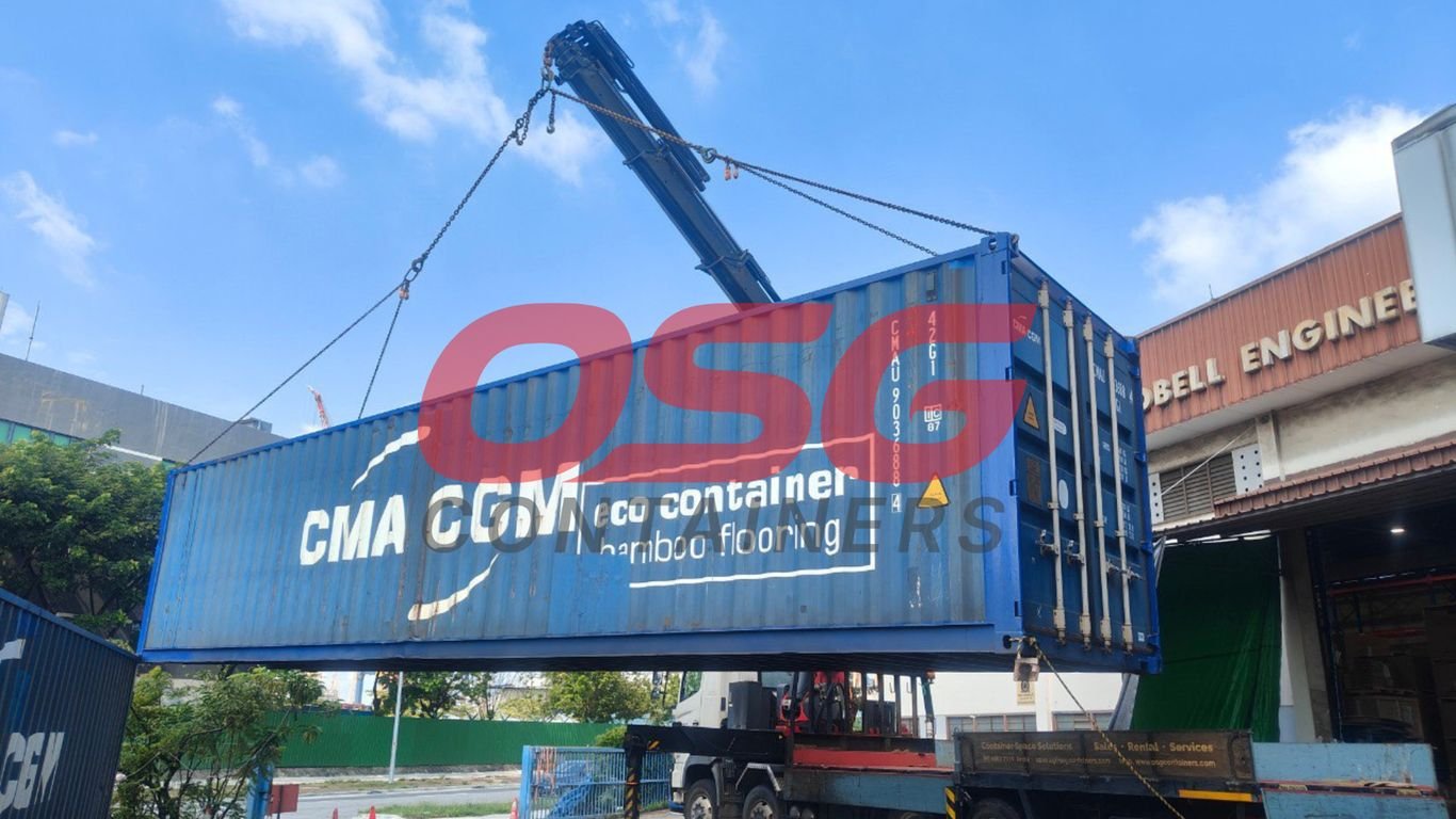 A crane lifts a blue shipping container onto a truck.