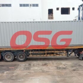 A large gray shipping container is loaded onto a truck.