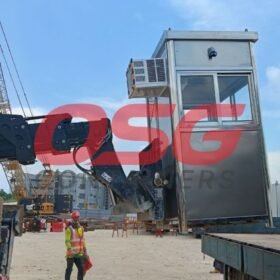 A crane lifts a portable security booth at a construction site.