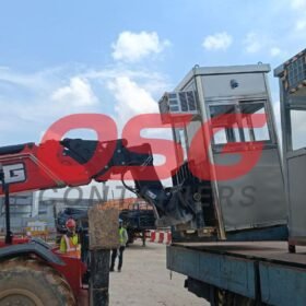 A crane lifts a security booth onto a truck at a construction site.