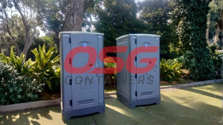 Two portable toilets are set up outdoors with lush greenery.